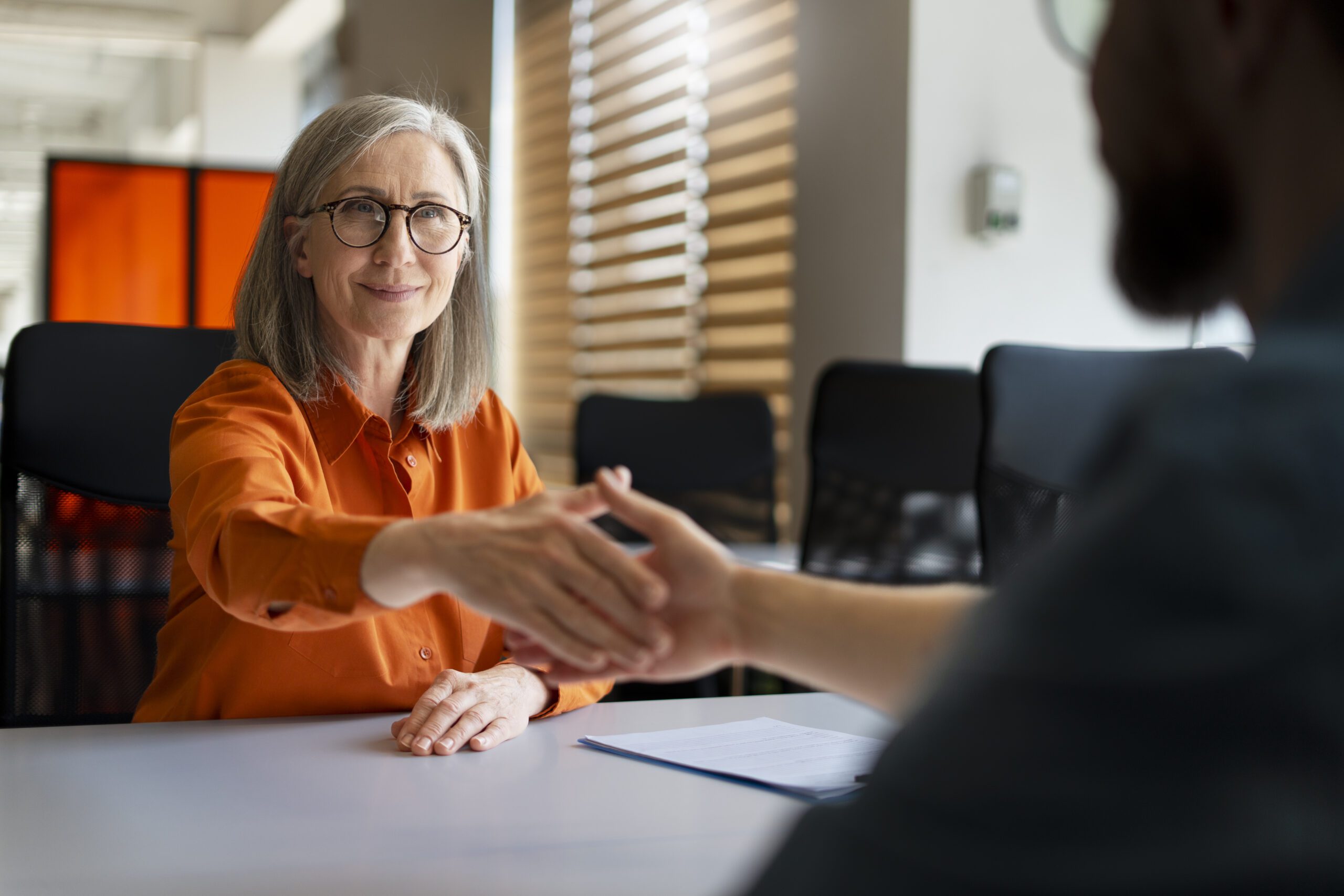 Professional woman shaking hands with a man, symbolizing trust and partnership in trustee services.